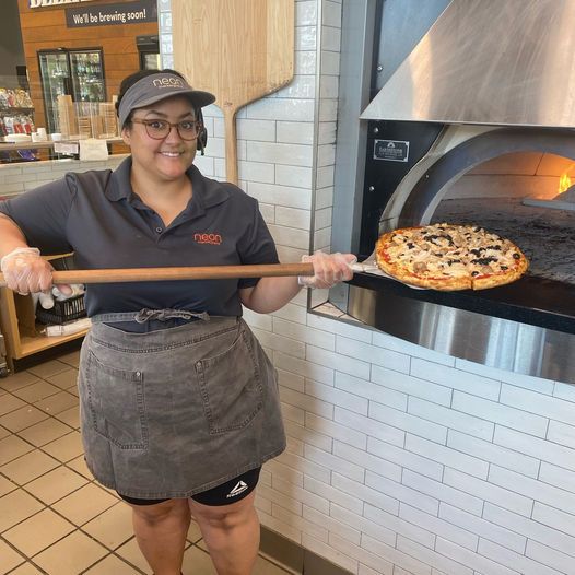 A photo of a person using a wooden paddle to take a pizza out of an oven.